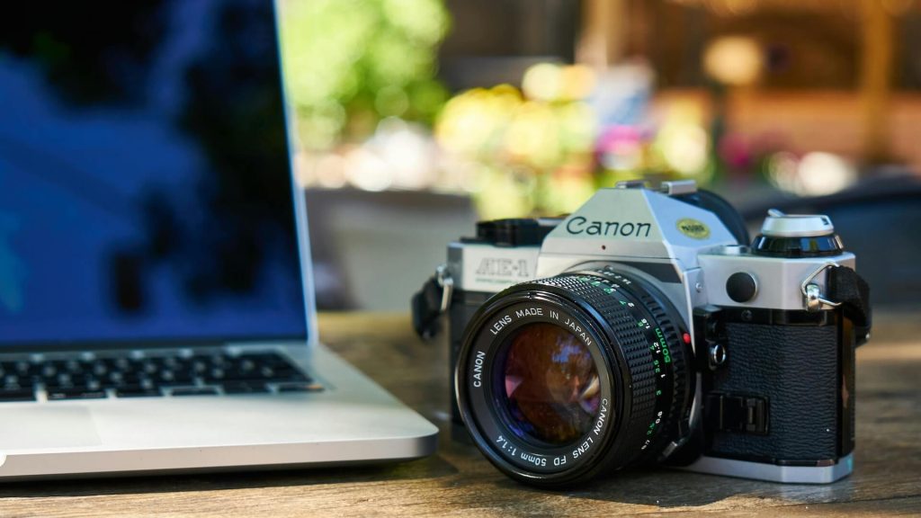 A camera sitting on a table next to a laptop; Screenwriting Basics: When to (And Not To) Write Camera Directions