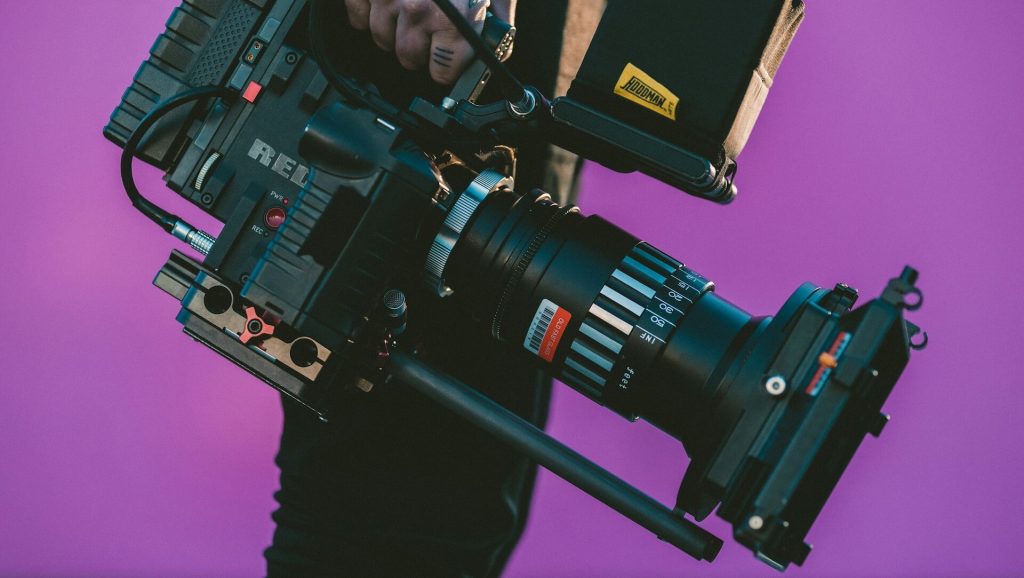 A man holding a film camera against a purple background