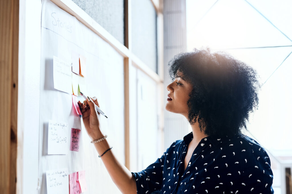 A woman with coiled hair in a black and white top looking a sticky notes on a wall; How 'Incoming' Screenwriters Transitioned from Staff Writers to Feature Filmmakers