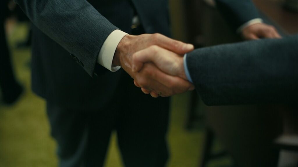 Two men in suits shaking hands in 'Oppenheimer' (2023)