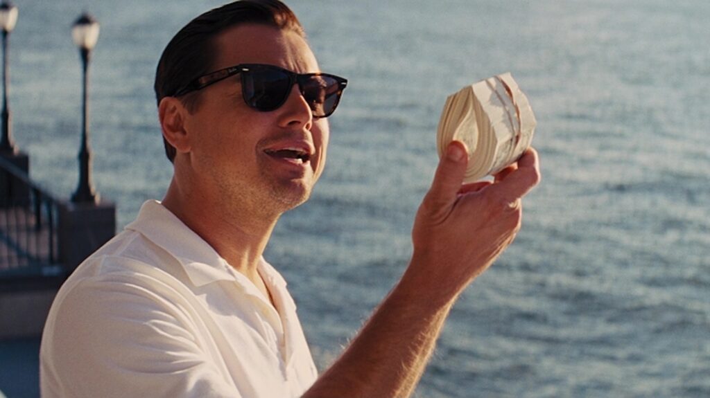 Jordan (Leonardo DiCaprio) holding money as he stands next to the ocean in 'The Wolf of Wall Street'