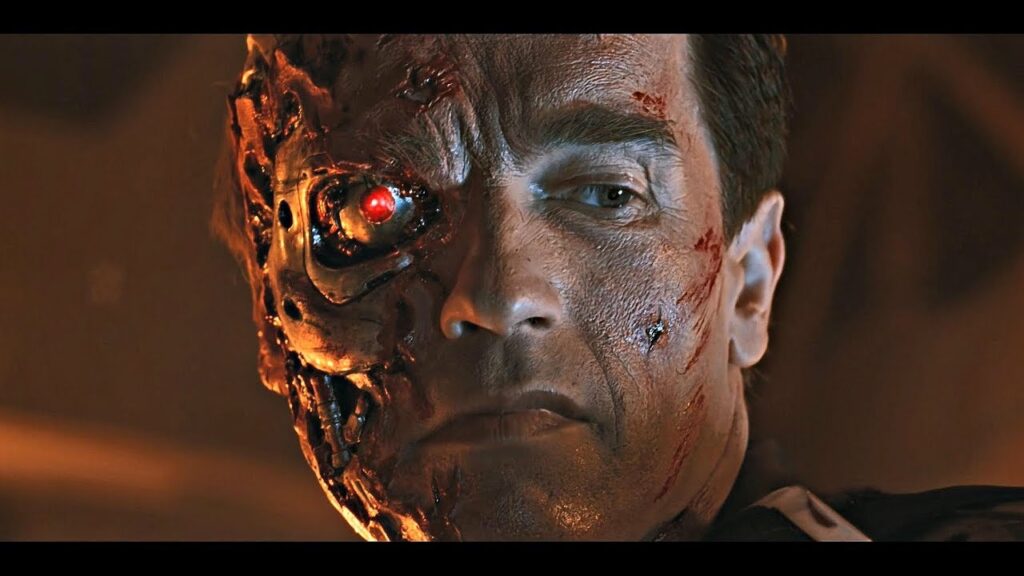 The Terminator (Arnold Schwarzenegger) with a burned face looking down at a destroyed machine in 'Terminator 2: Judgement Day'