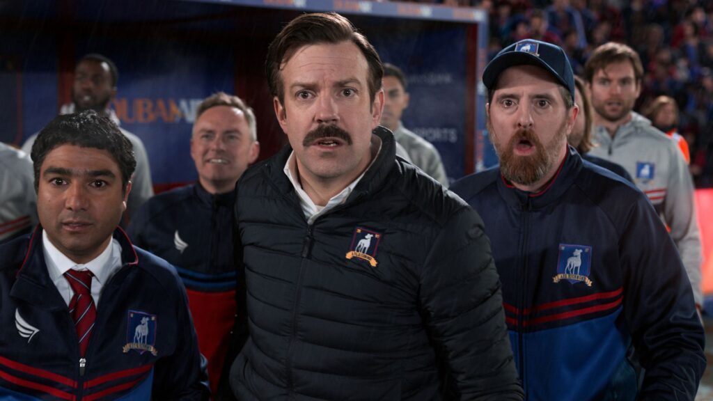 Ted Lasso (Jason Sudeikis) and the coaching staff watching a soccer match in 'Ted Lasso'