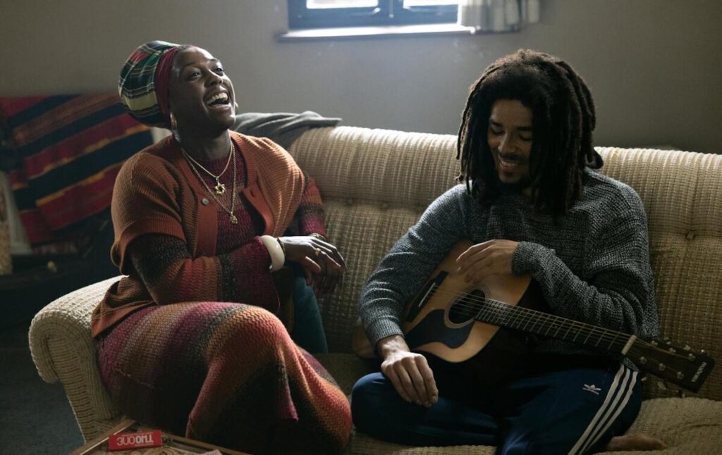 Bob Marley(Kingsley Ben-Adir) playing guitar on the couch in 'Bob Marley: One Love,' How to Write the Best Biopic