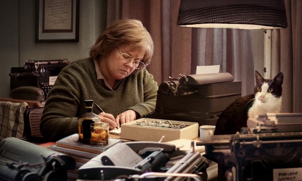 Lee Israel (Melissa McCarthy) writing on a desk covered in letters and books in 'Can You Ever Forgive Me'