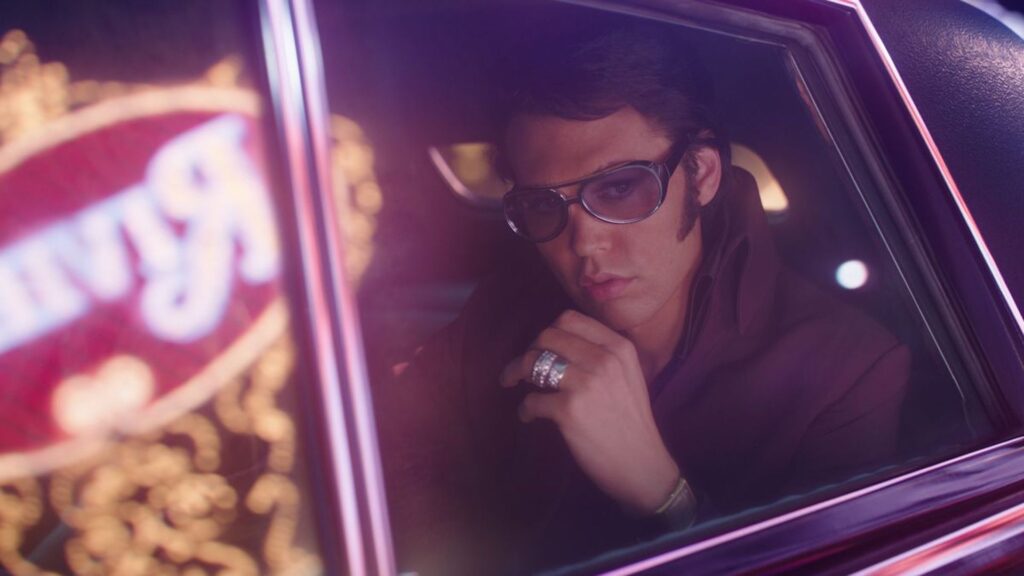 Elvis Presley (Austin Butler) sitting in a leather jacket in the backseat of a car in 'Elvis'