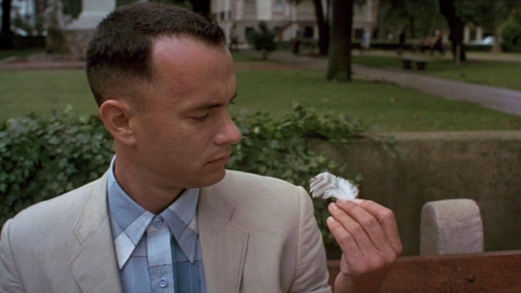 Forrest (Tom Hanks) in a tan suit looking at a feather in 'Forrest Gump,' 100 Symbolism Prompts for Stories