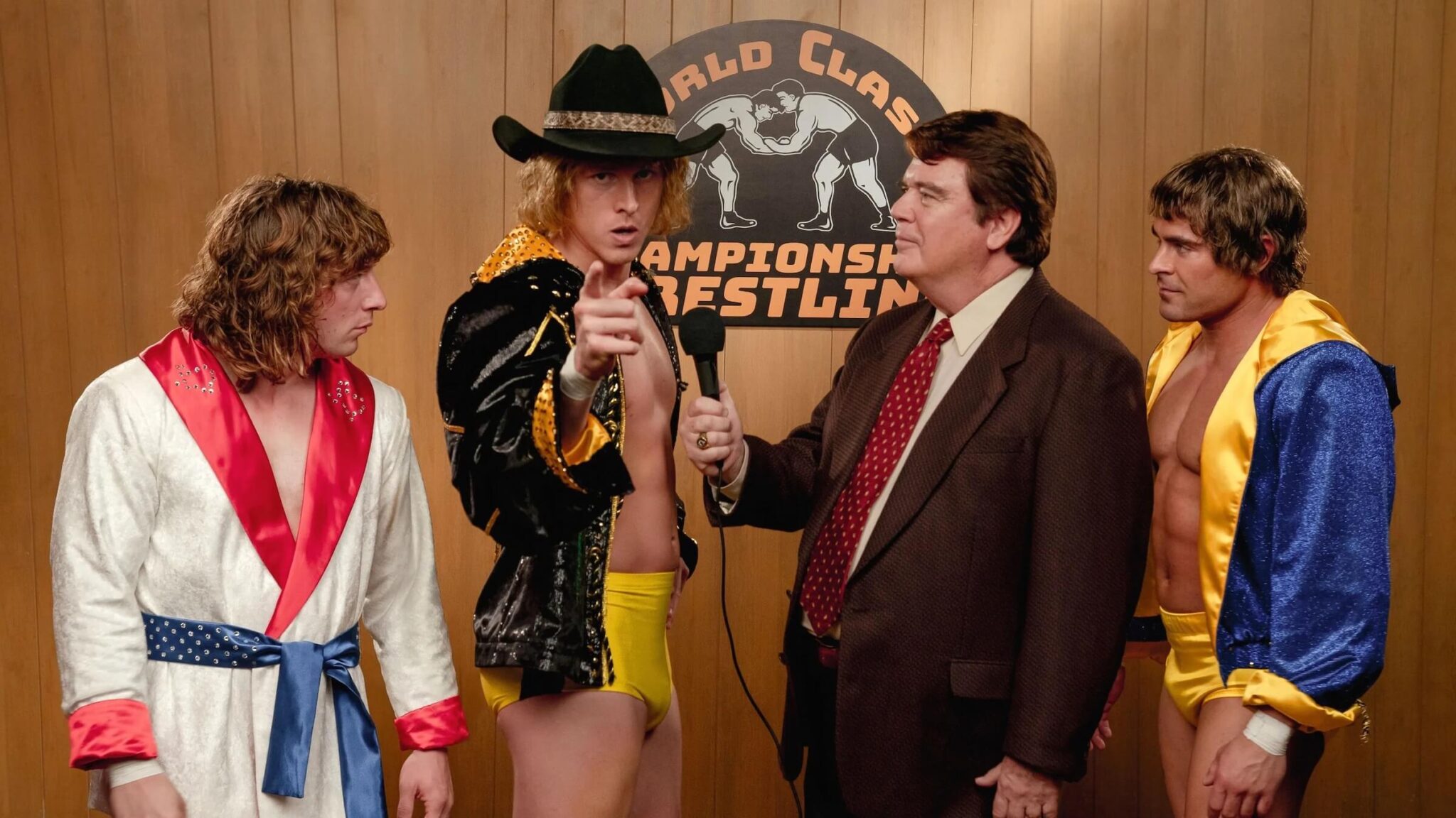 (L-R) Kerry (Jeremy Allen White), David (Harris Dickinson), and Kevin Von Erich (Zach Efron) talking into a camera in 'Iron Claw,' How to Write the Best Biopic