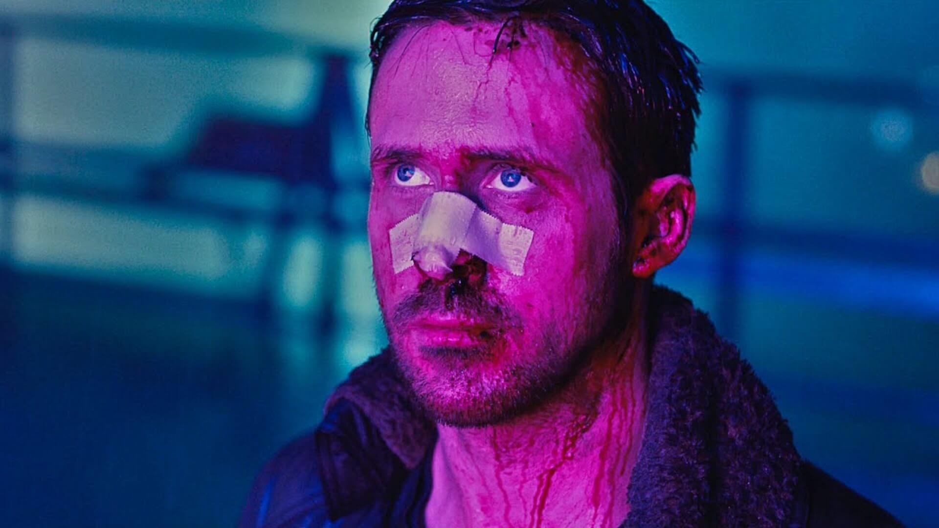 K (Ryan Gosling) with a bandage over his nose while looking at a hologram in 'Blade Runner 2049,' 5 Trademarks of Denis Villeneuve Movies