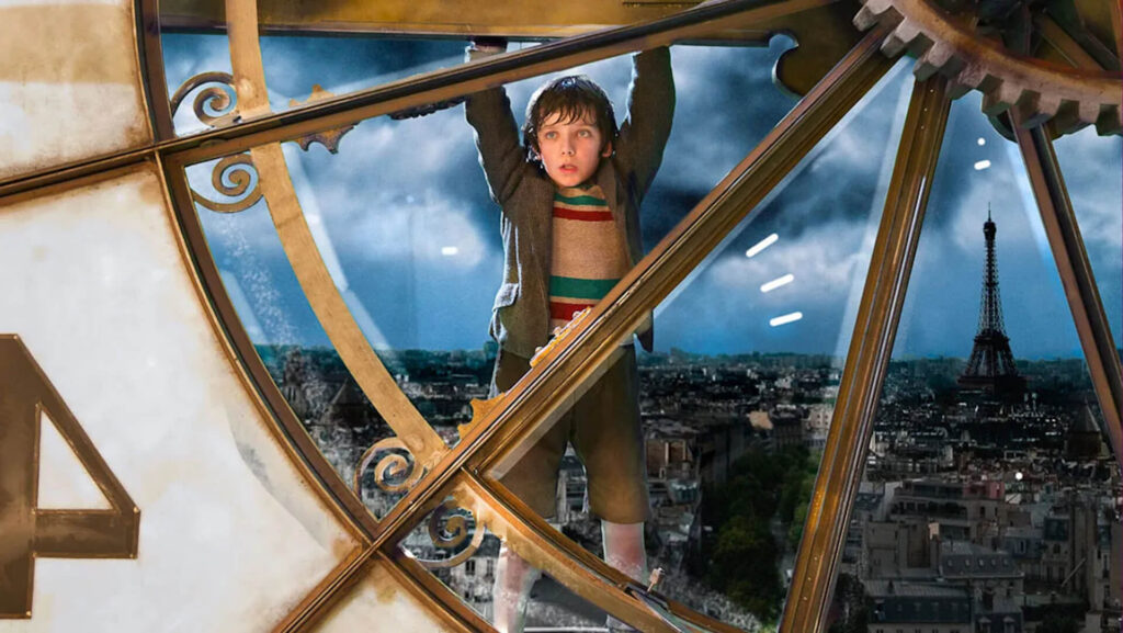 Hugo Cabret (Asa Butterfield) hanging from a clock in Paris in ‘Hugo’