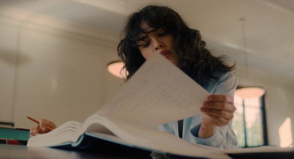 A woman with dark curly hair reading a book in 'I Care A Lot,' The Do’s and Don'ts of Writing Professional Script Coverage