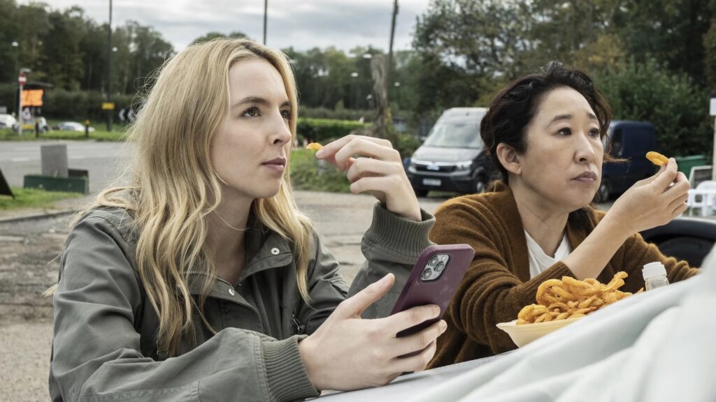 Eve Polastri (Sandra Oh) and Villanelle (Jodie Comer) eating food while looking over the hood of a car in 'Killing Eve'