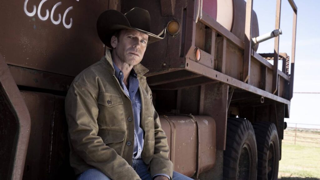 Taylor Sheridan in a cowboy hat sitting next to a large farm truck, How Taylor Sheridan Redefined the Western Genre With His Own Stories