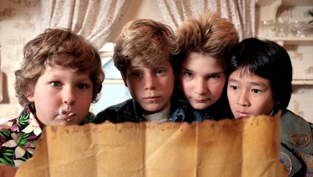 Chunk (Jeff Cohen), Mikey (Sean Astin), Mouth (Corey Feldman), and Data (Ke Huy Quan) looking a treasure map in 'The Goonies,' Breaking Down the Character Archetypes of the Hero’s Journey