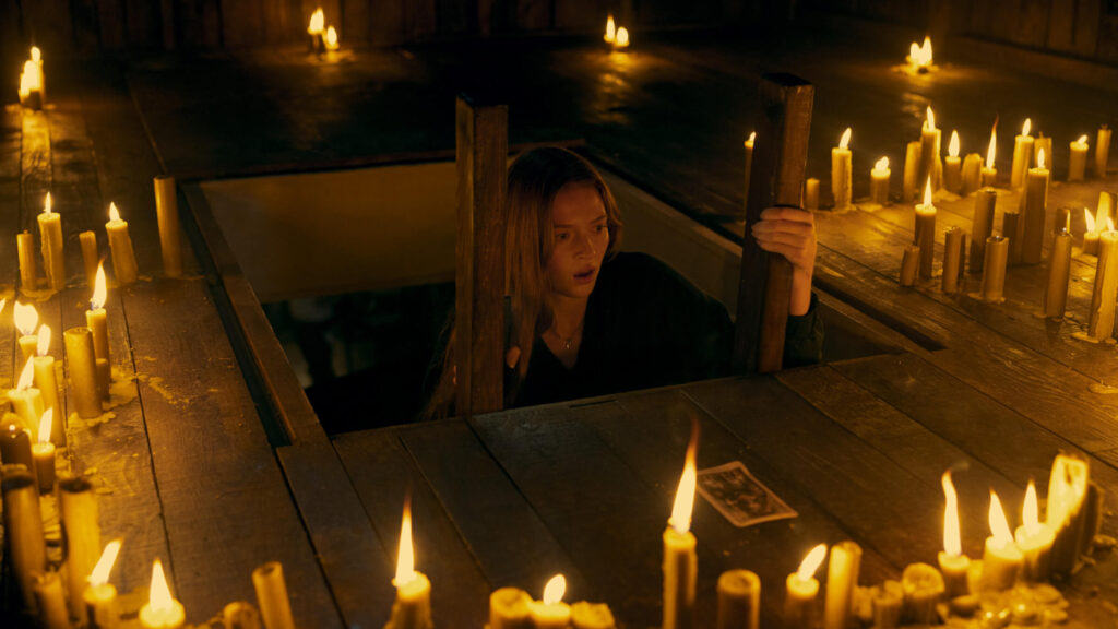 A woman with blonde hair climbs a ladder into an attic full of candles and a Tarot card in 'Tarot,' From Concept to the Screen: 5 Lessons from 'Tarot' Creators
