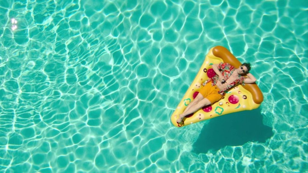 Nyles (Andy Samberg) floating on a pizza shaped floaty in a pool in 'Palm Springs,' 7 Signs You Have a Good Story Idea