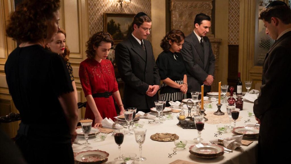 A family praying around a dinner table in 'We Were The Lucky Ones,' How ‘We Were The Lucky Ones’ Showrunner Erica Lipez Masterfully Adapted the Complex Narrative for TV