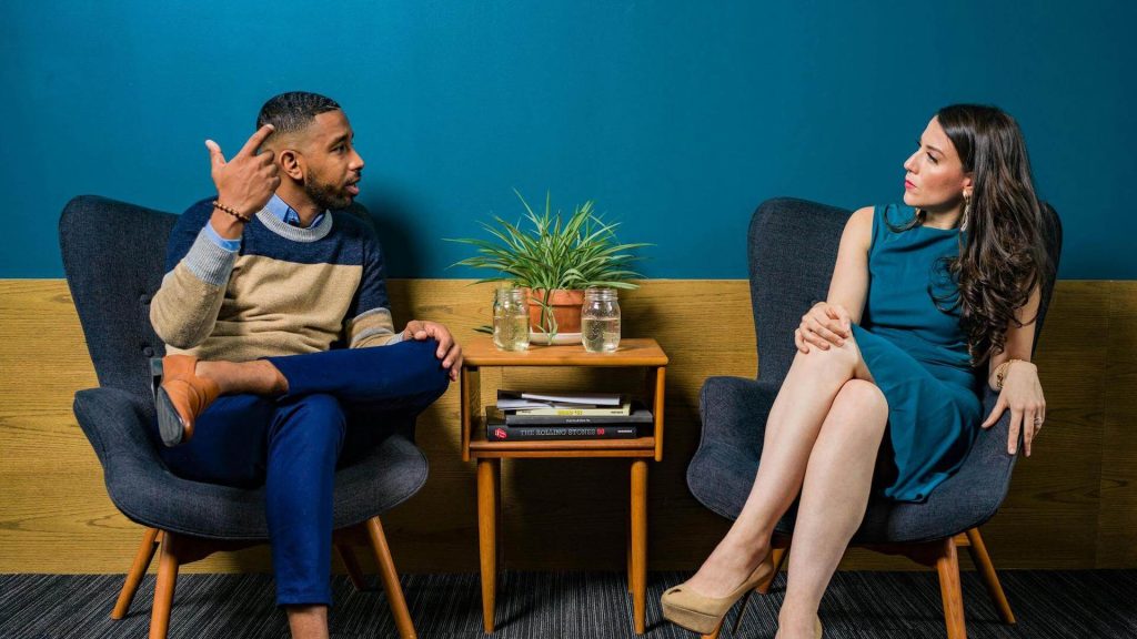 Woman Wearing Teal Dress Sitting on Chair Talking to Man