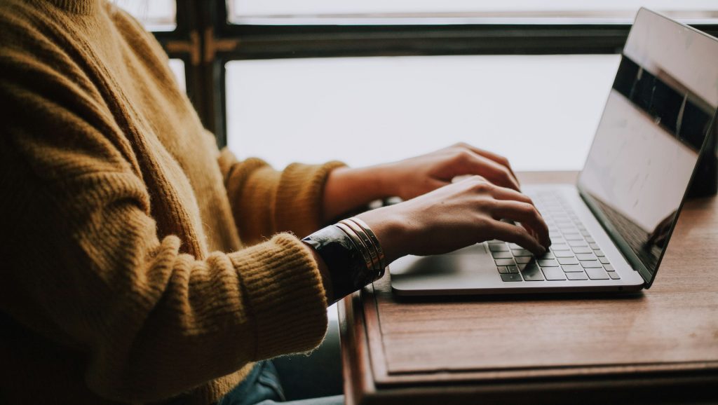 A person in a yellow sweater typing on a laptop