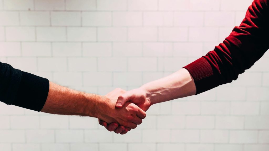 Two people shaking hands in front of a white brick wall; How I Landed 10 Feature Script Deals in Four Years (Without an Agent)