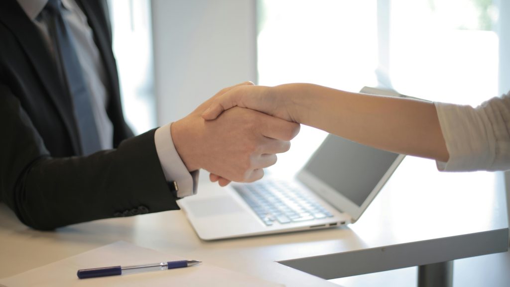 Two people shaking hands over an open laptop in an office during the day