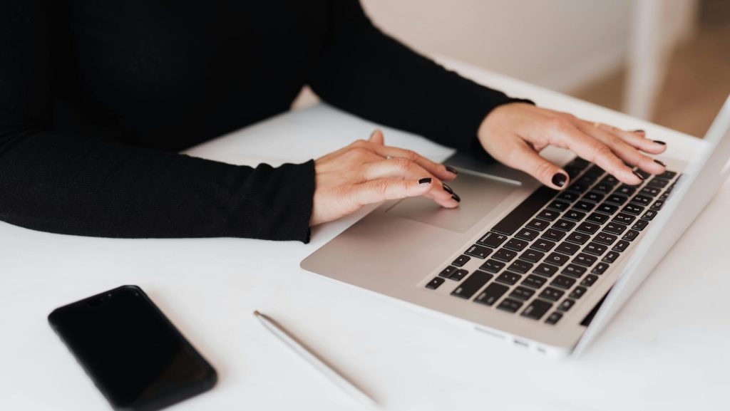 A woman with black nail polish typing on a silver laptop; 5 Questions To Ask Yourself When Getting Script Notes