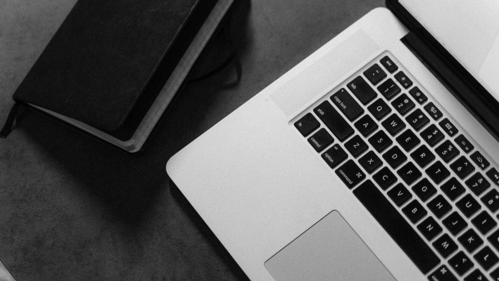 A laptop and a notebook against a black desk