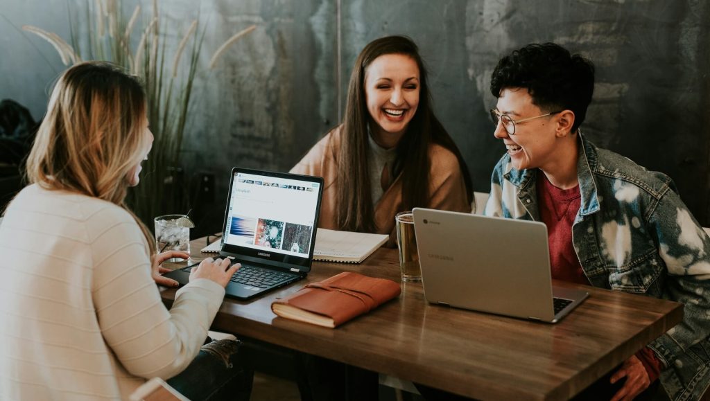 Three people sitting in front of computers laughing