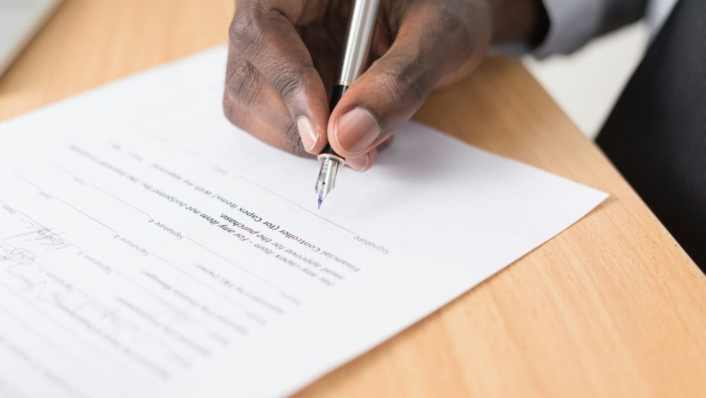 A hand holding a pen about to sign a contract