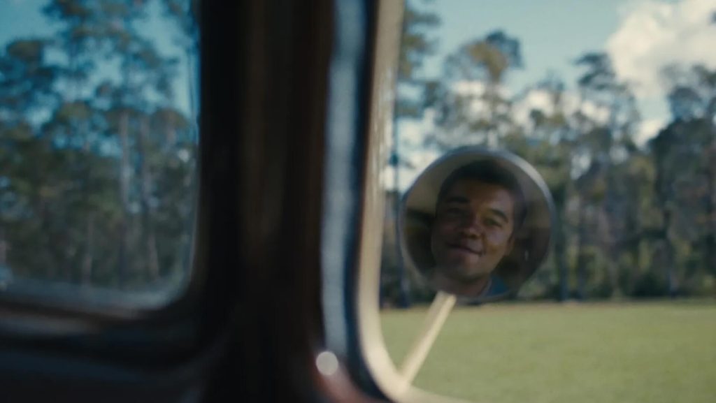 Elwood (Ethan Herisse) smiling in a passenger side mirror in 'Nickel Boys.'