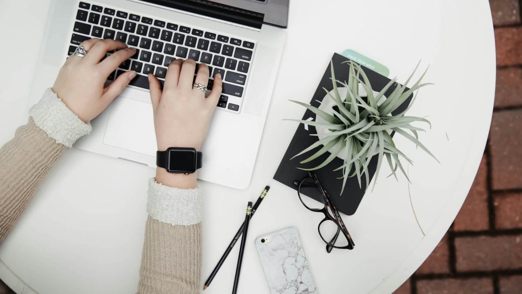 A person typing on a silver laptop on a white table; How to Be a Pro Screenwriter Without Representation