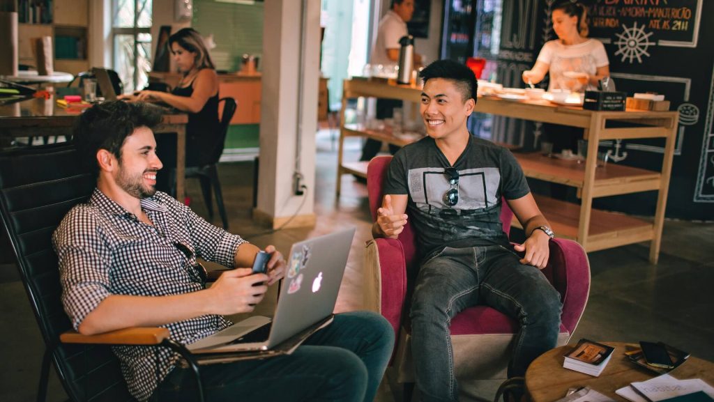 Two men sitting down in a coffee shop talking to each other 