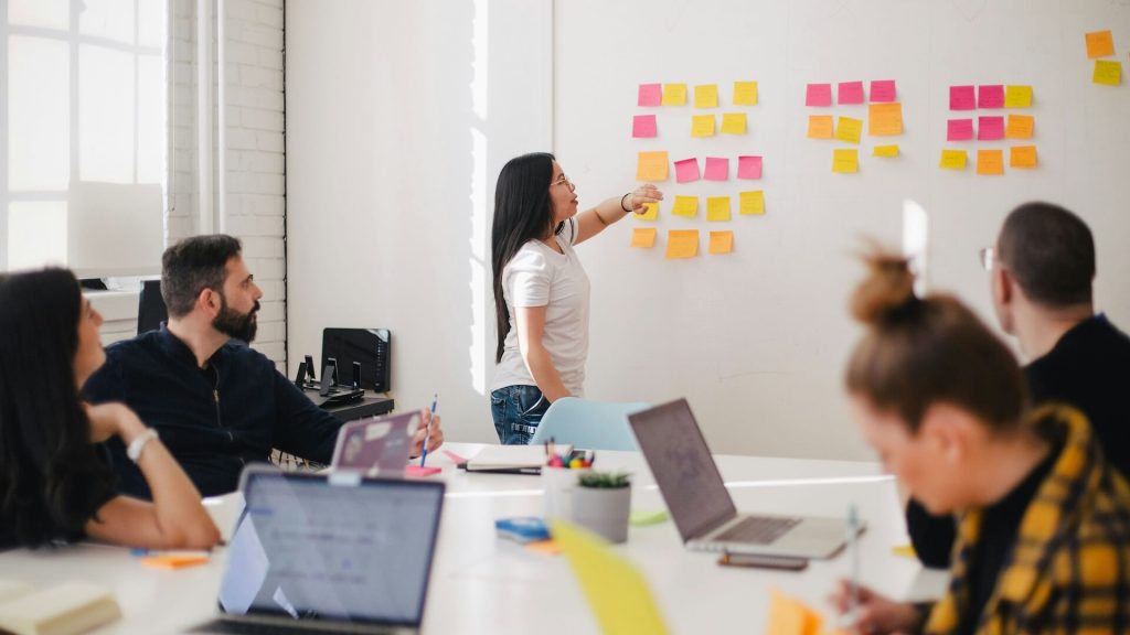 A woman pointing to sticky notes on a white board during a meeting.